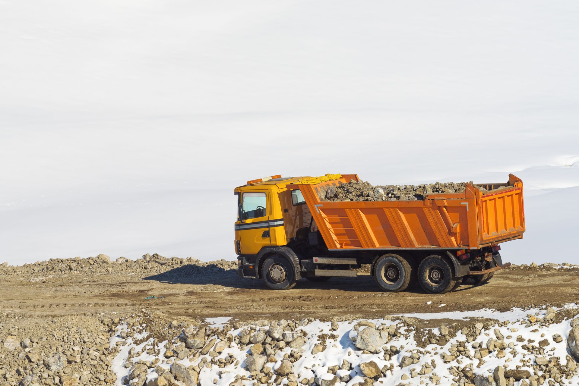 Orange dump truck hauling dirt on a barren construction site under a pale sky