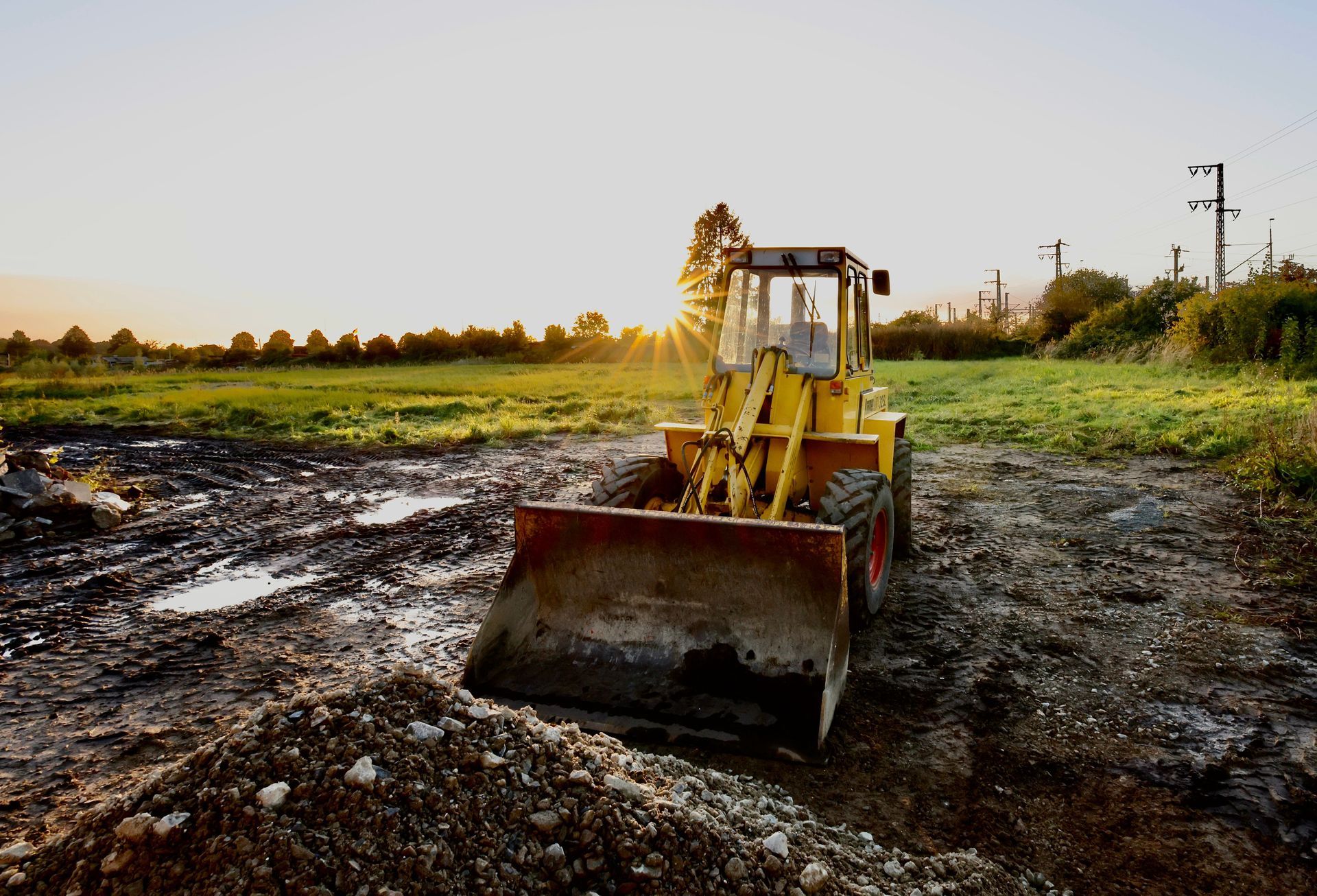 Yellow bulldozer working on muddy construction site at sunset with grassy field in the background