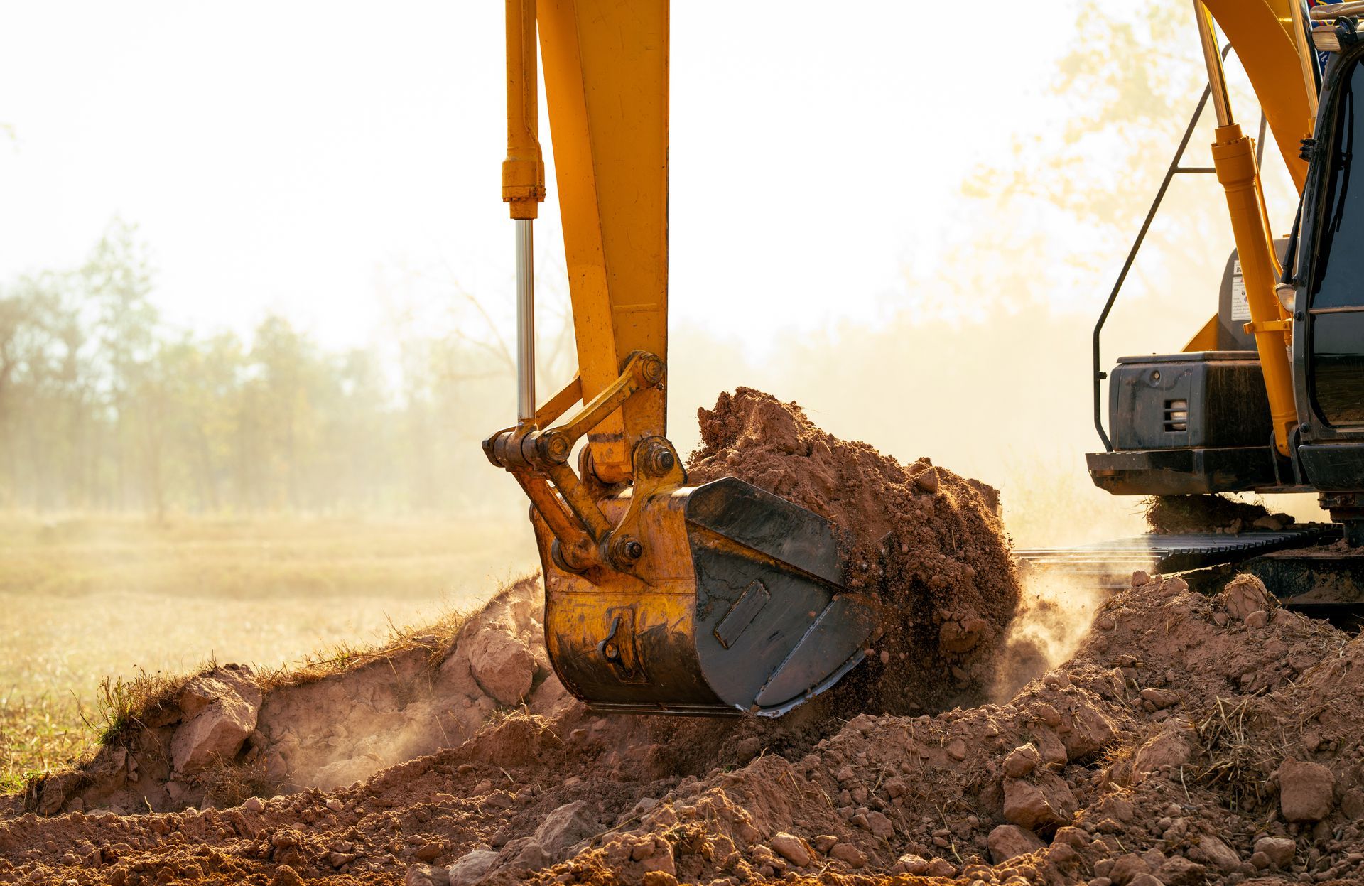 Excavator digging a dirt pile at a construction site in a dusty field