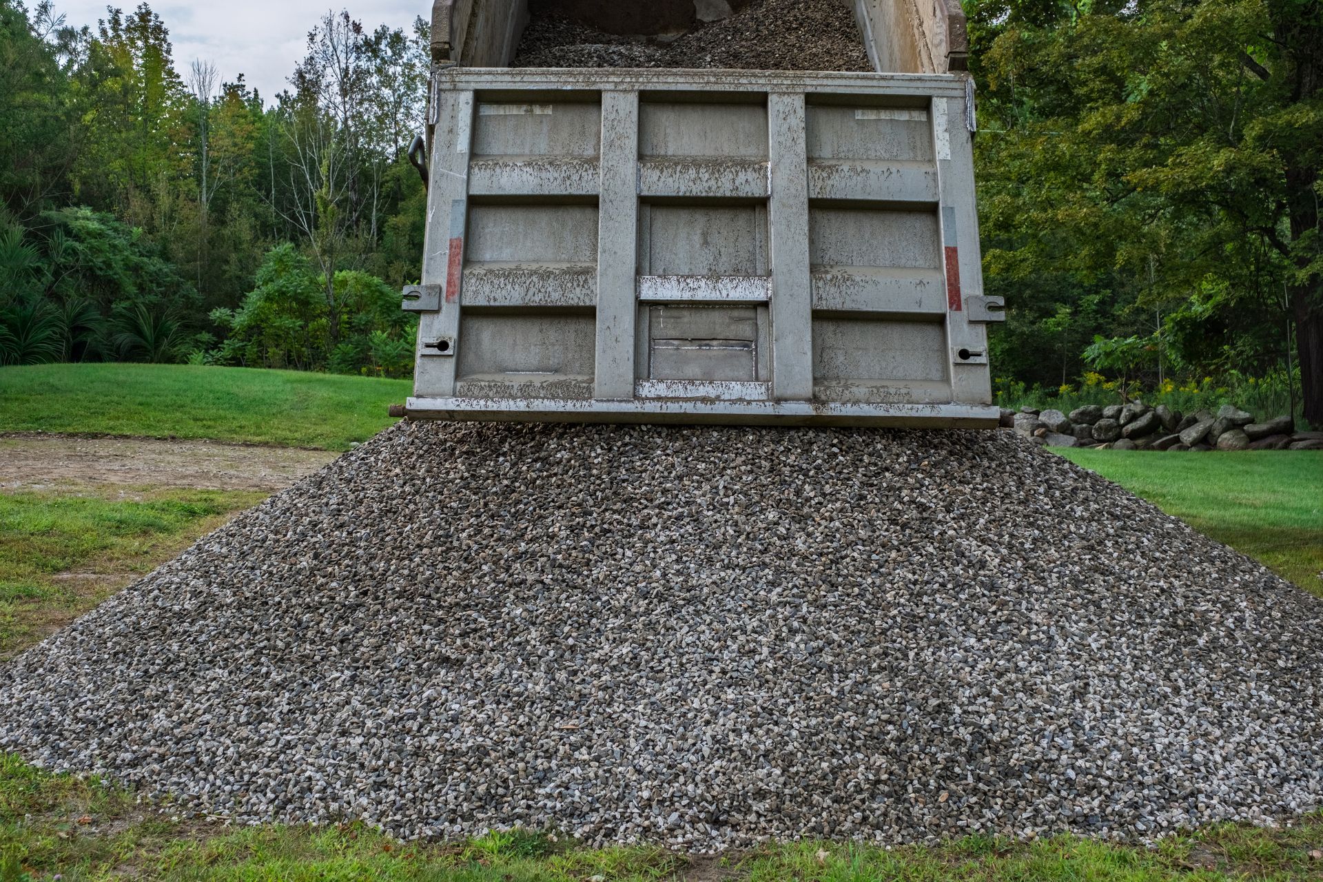 Gravel mound beneath a concrete chute in a grassy park, with trees in the background