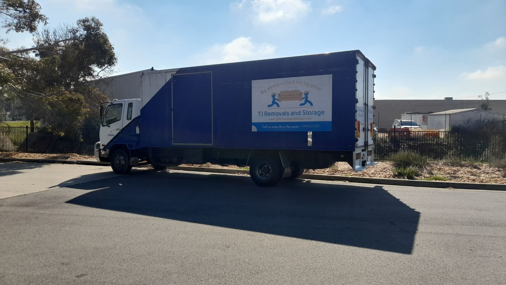 Blue cargo truck parked on a street beside a building in bright sunlight — TJ Removals and Storage in Wagga Wagga, NSW