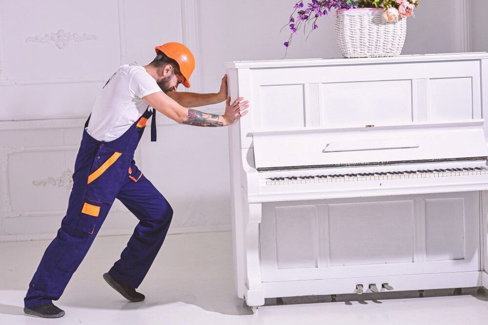 A Man is Pushing a White Piano in a Room — TJ Removals and Storage in Wagga Wagga, NSW
