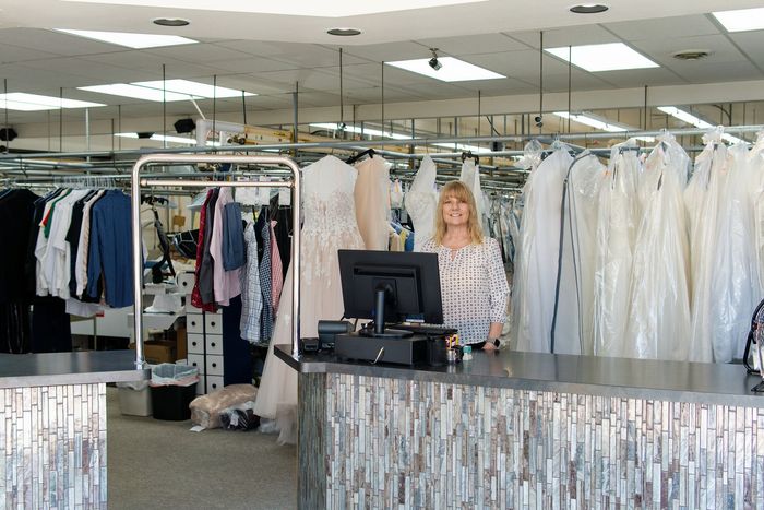 Country Cleaners employee at the front counter surrounded by professionally cleaned and bagged garments.