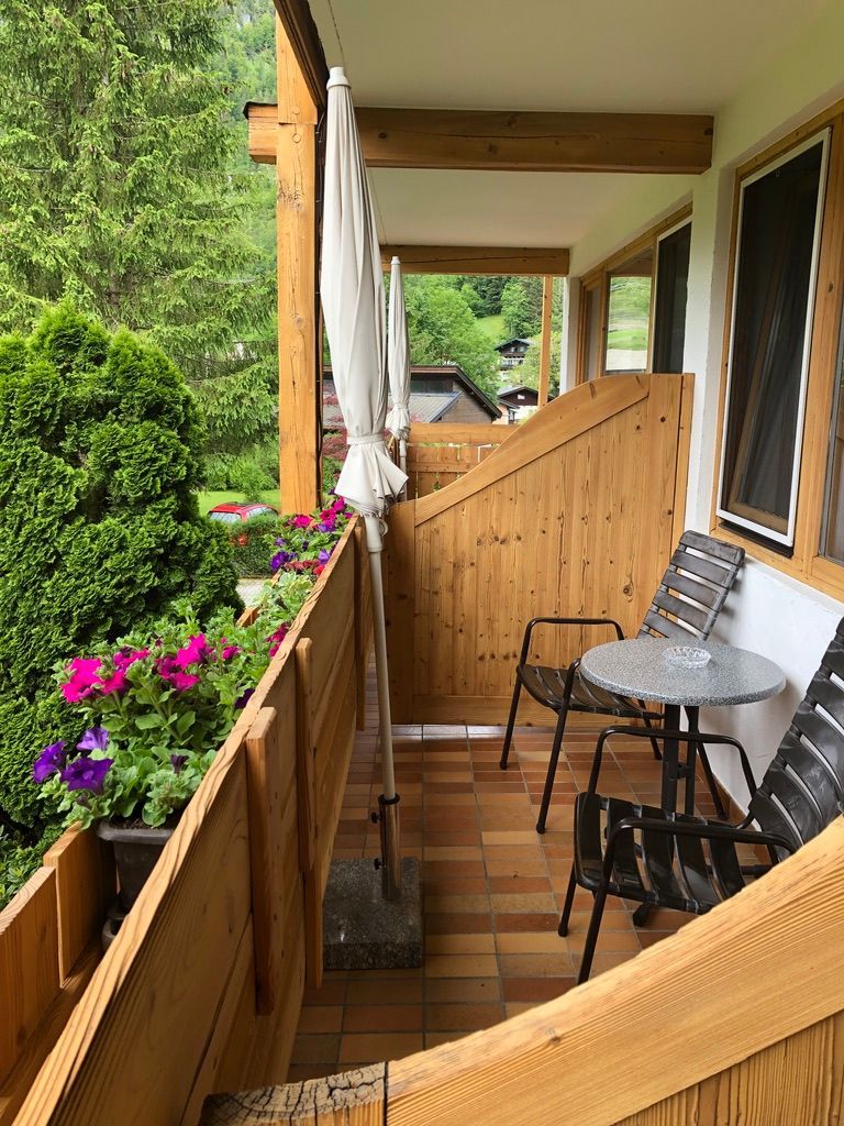 Balkon einer Holzwohnung mit Topfblumen, Stühlen und einem kleinen Tisch mit Blick ins Grüne