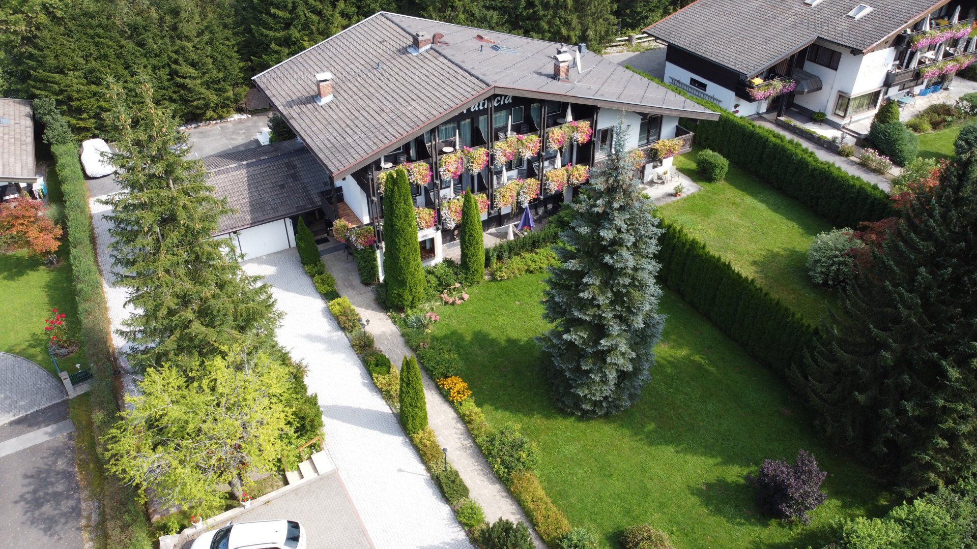 Luftaufnahme eines Hauses mit einer gut besuchten Gartenparty, Sitzgelegenheiten auf der Terrasse und einem grünen Rasen.