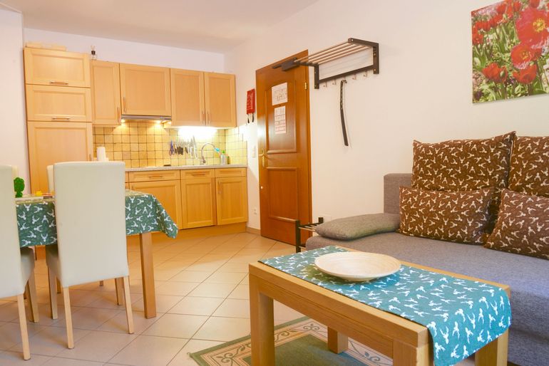 Helle Wohnküche mit Holzschränken, Tisch und einem braunen Sofa an einer Fensterwand