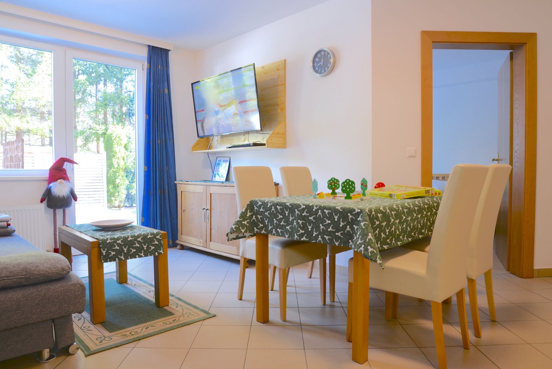 Helles Wohn-Esszimmer mit Tisch, Stühlen, Sofa, Fernseher und Sonnenlicht durch Glastüren
