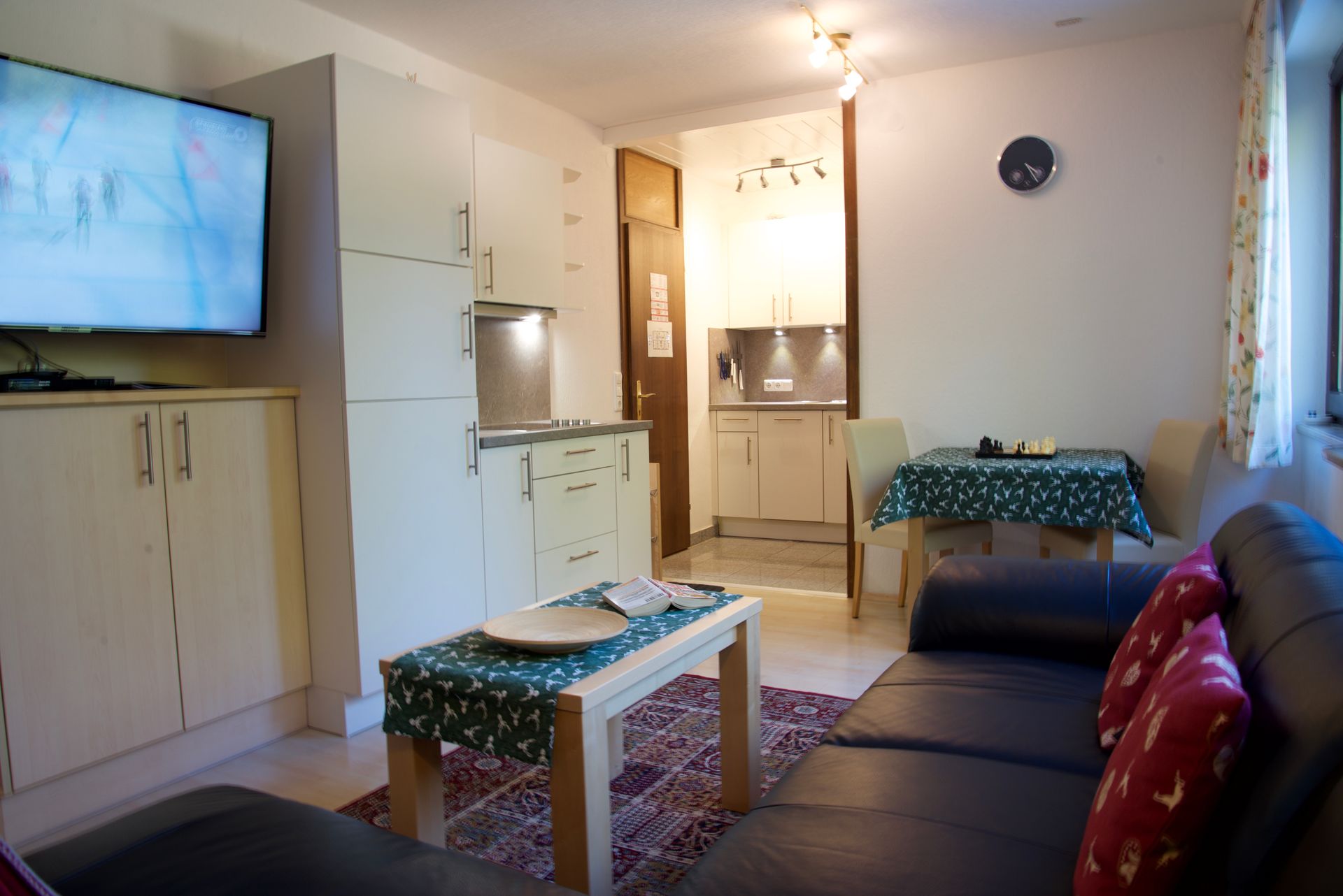 Kompaktes Wohnzimmer mit Fernseher, Sofa, Couchtisch und kleiner Küche im Hintergrund