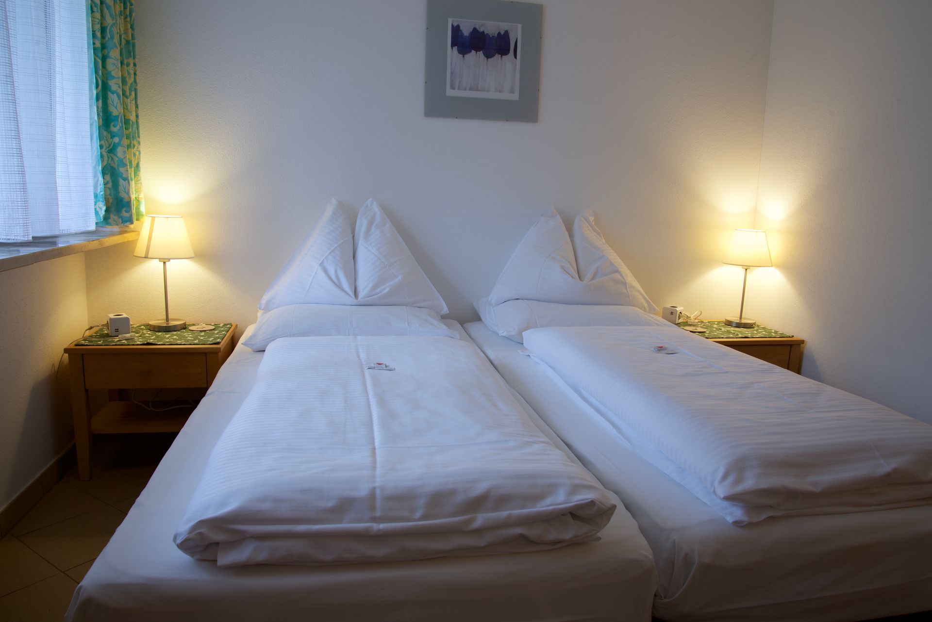 Ein Doppelbett in einem sanft beleuchteten Hotelzimmer mit Nachttischlampen und weißer Bettwäsche.