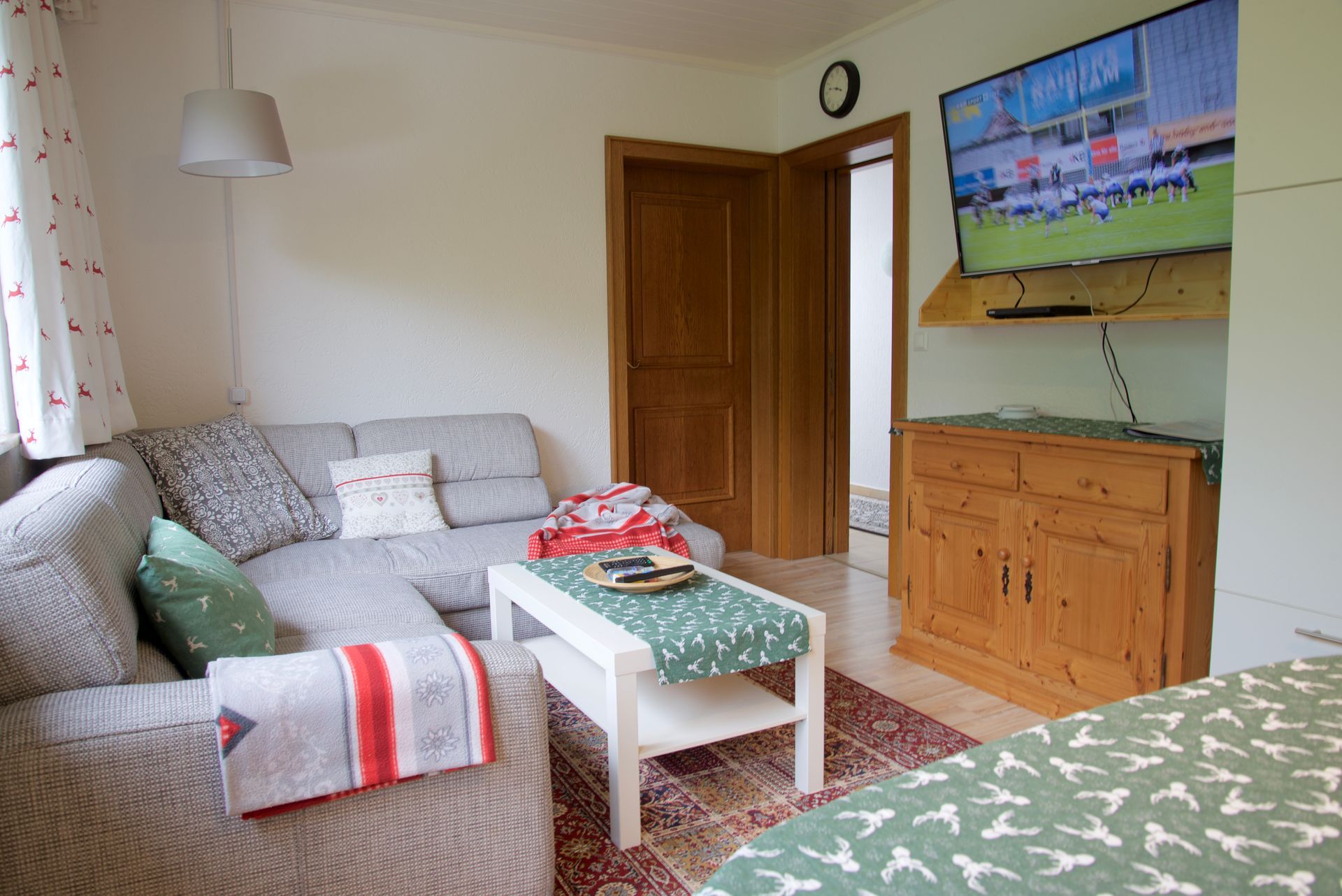 Gemütliches Wohnzimmer mit grauen Sofas, Couchtisch, Holzschrank und darüber montiertem Fernseher.