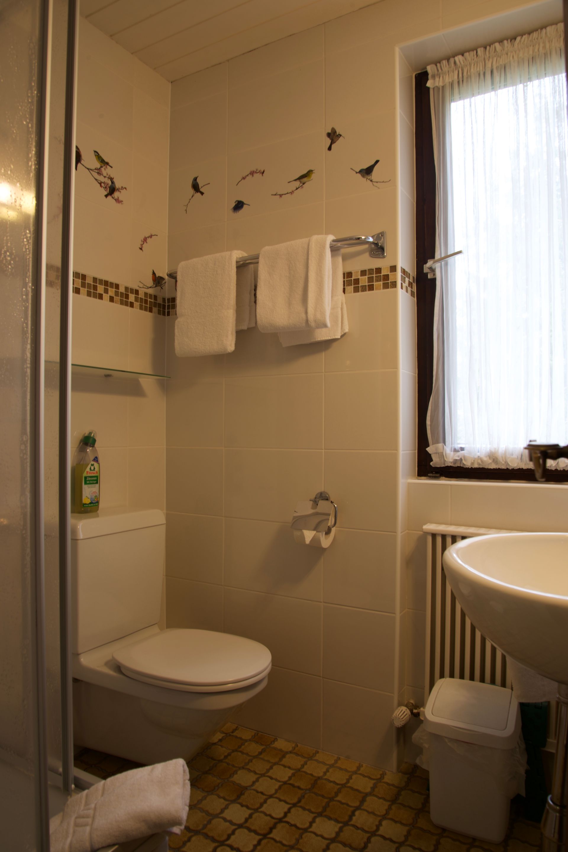 Kleines Badezimmer mit Toilette, Waschbecken, Handtuchhalter, Heizkörper und Fenster über einer Heizkörperverkleidung.