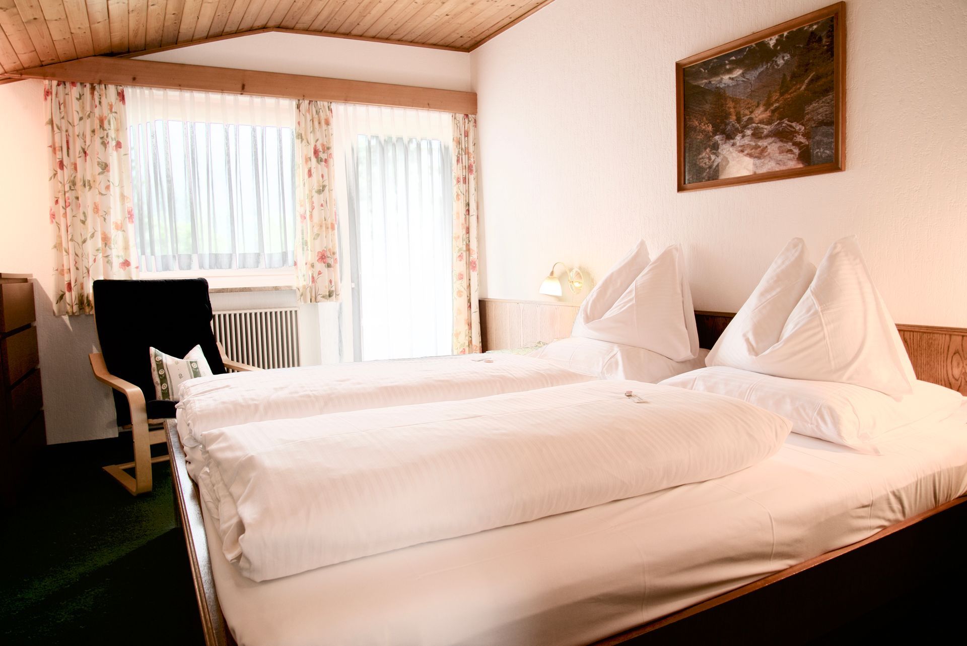 Hotelzimmer mit einem Doppelbett, einem Fenster, einem Schreibtisch und einem Stuhl in warmen Farbtönen.