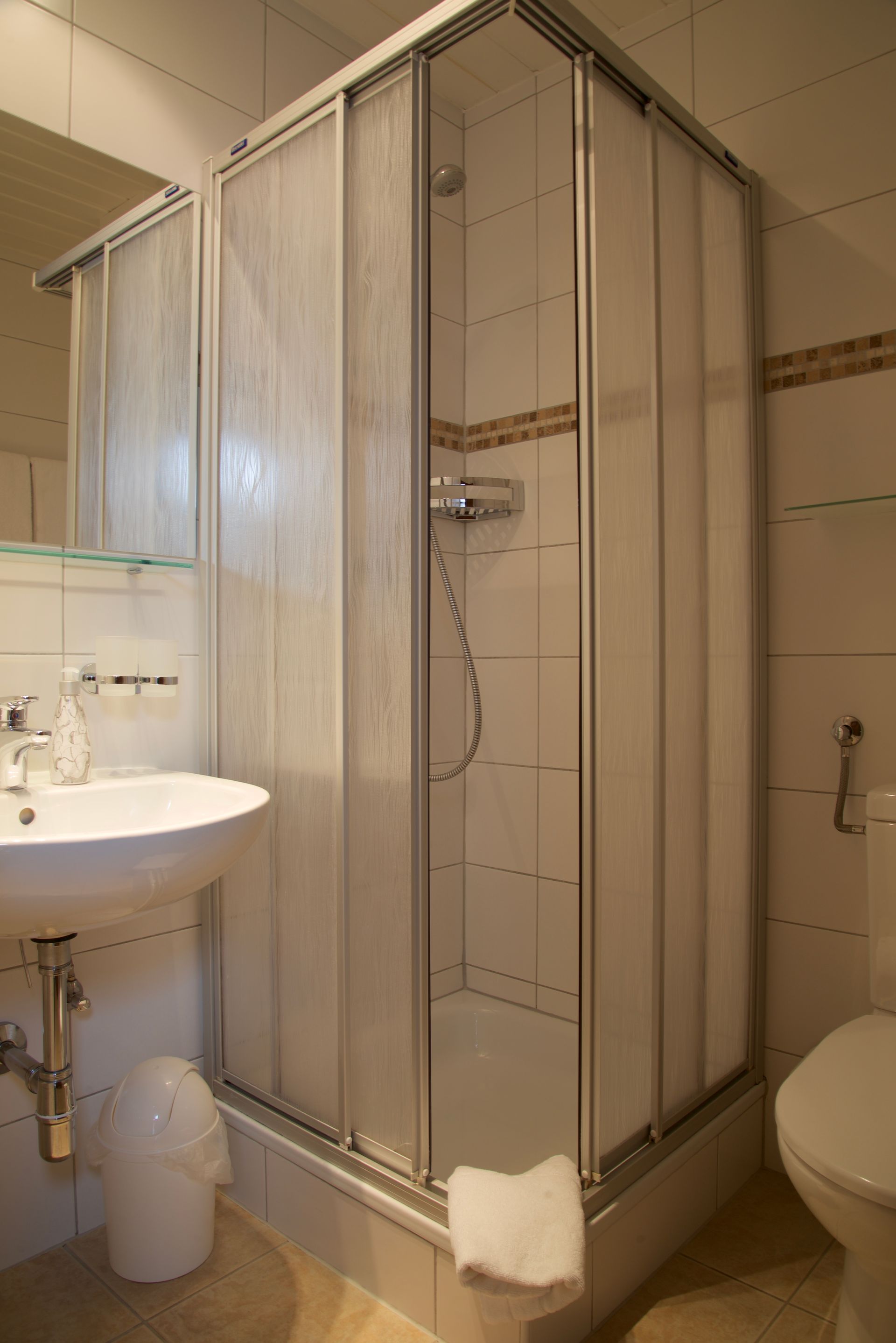 Kleines Badezimmer mit verglaster Dusche, Waschbecken links und Toilette rechts.