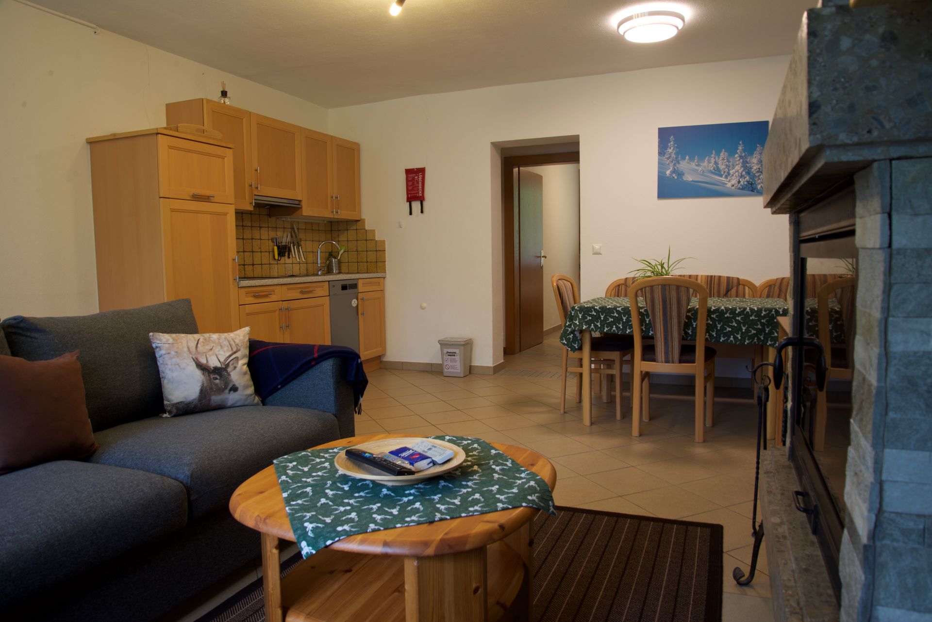 Wohnzimmer mit dunklem Sofa, rundem Couchtisch, Essgruppe, Holzschränken und Kamin