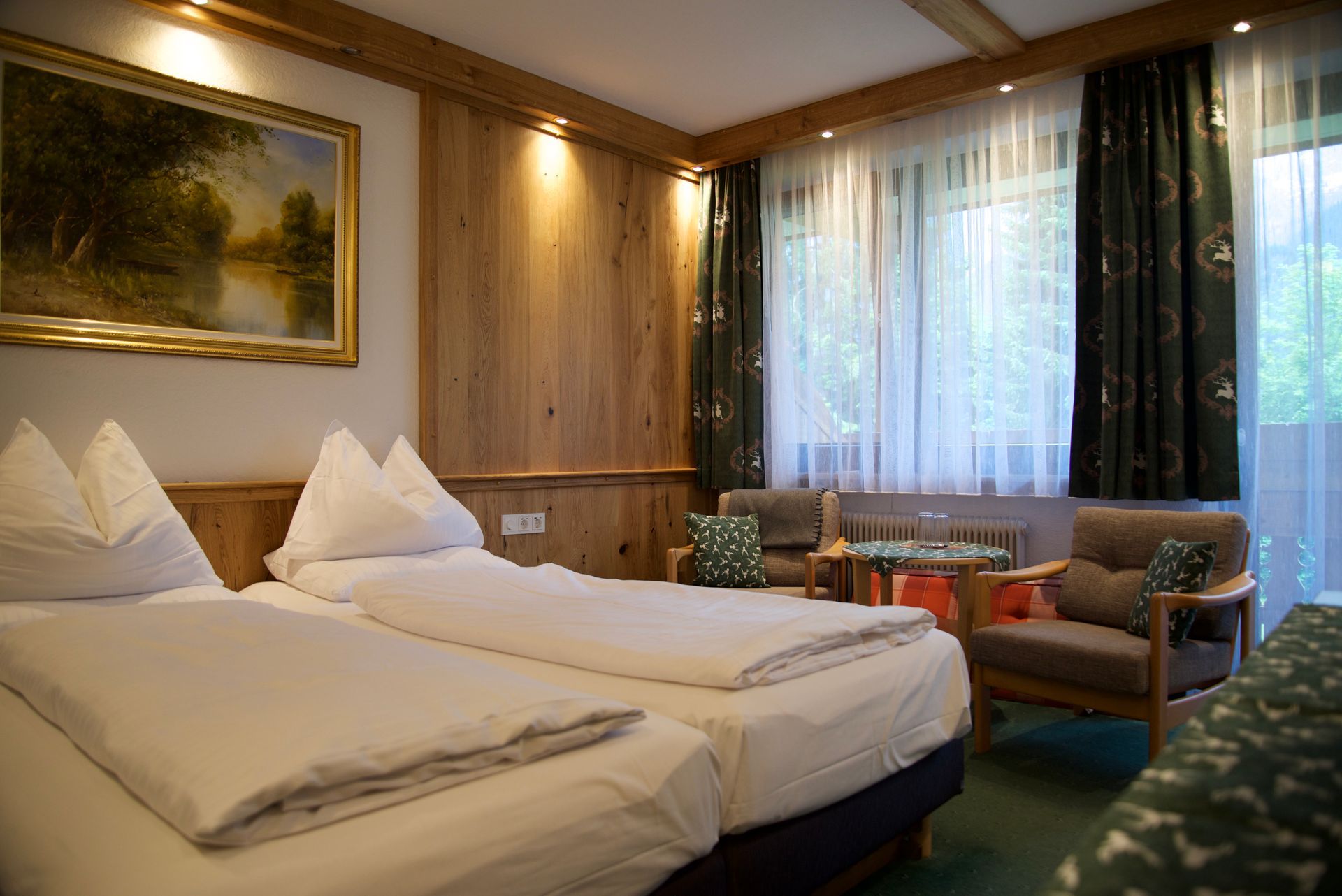 Hotelzimmer mit zwei Betten, holzgetäfelten Wänden, einem Fenster und einer Sitzecke mit Stühlen und einem Tisch.