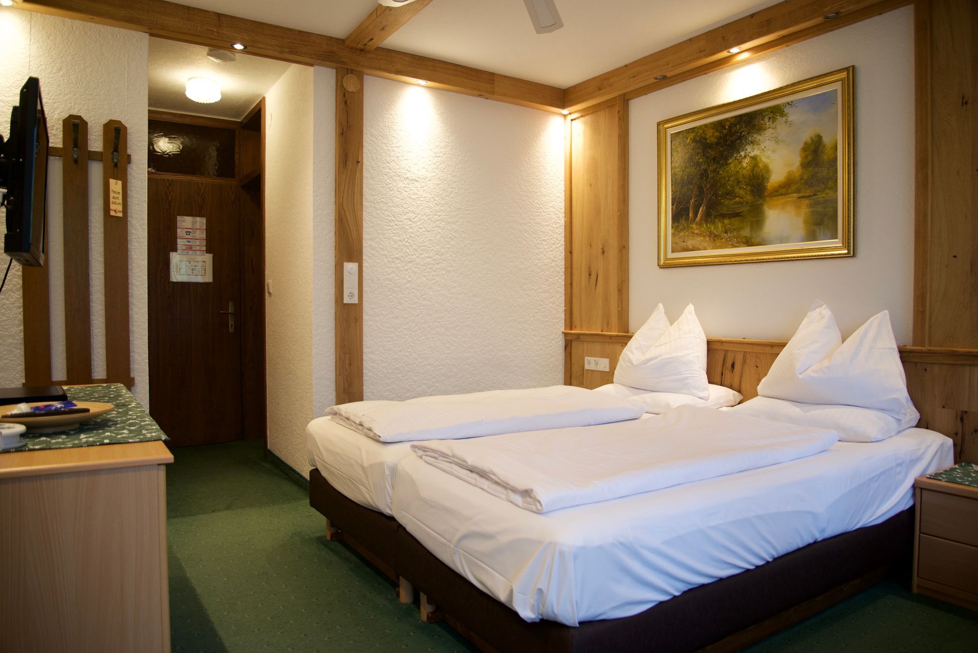 Hotelzimmer mit zwei Einzelbetten, grünem Teppich, Holzmöbeln und gerahmten Wandbildern.