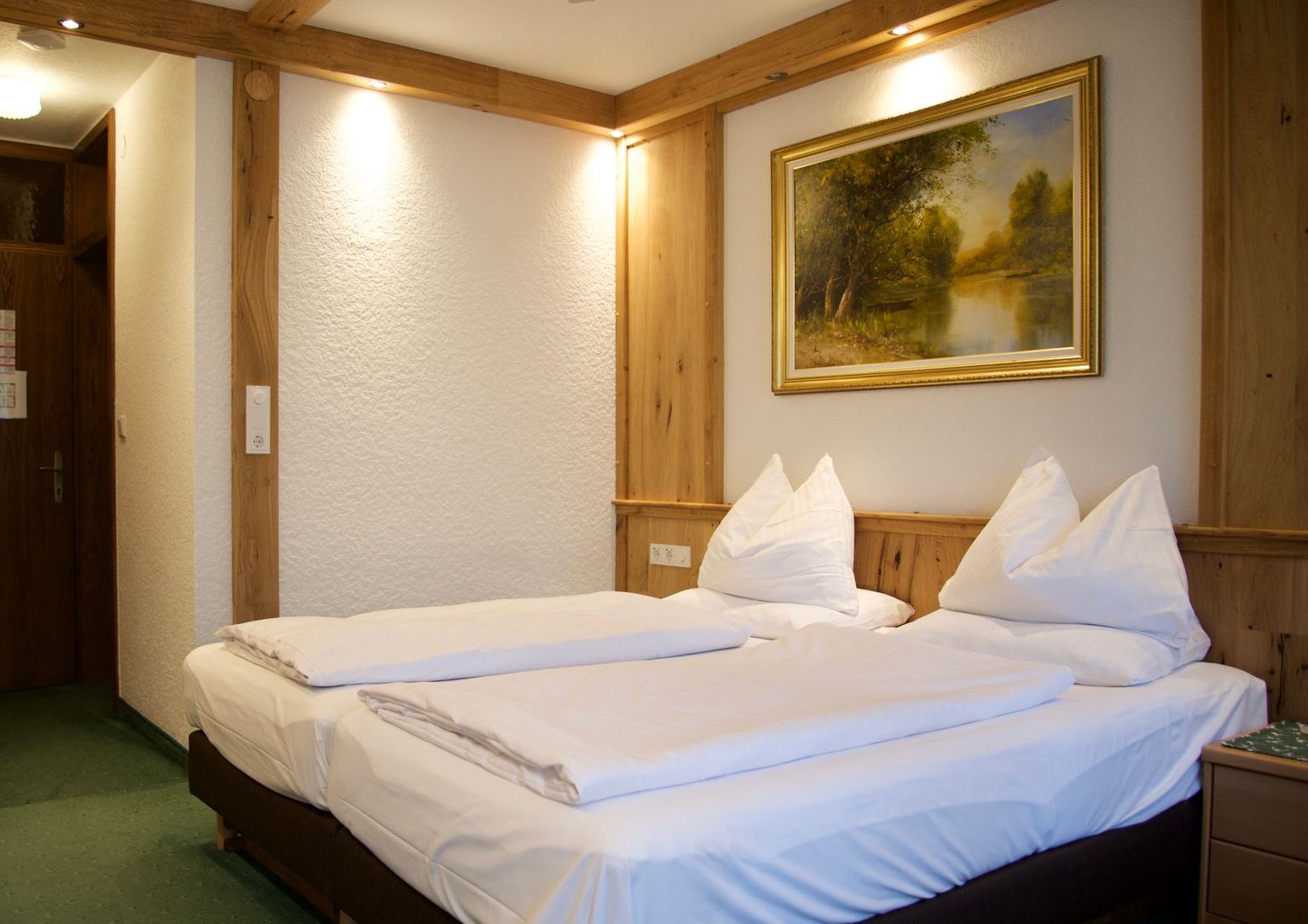 Hotelzimmer mit zwei ordentlich gemachten Einzelbetten, Holzvertäfelung und gerahmtem Landschaftsgemälde