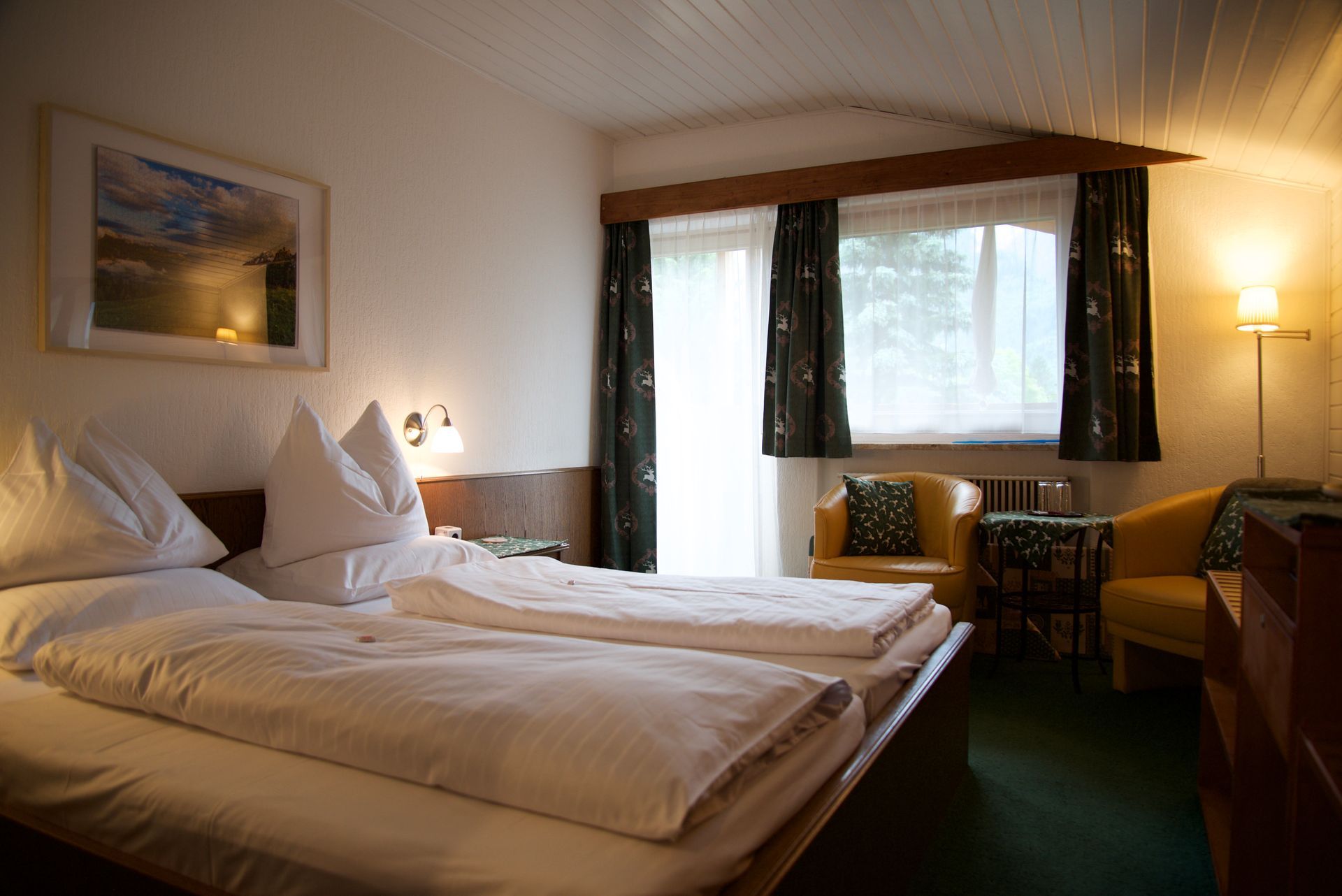 Hotelzimmer mit zwei Einzelbetten, Fenster, Schreibtisch und warmem Lampenlicht
