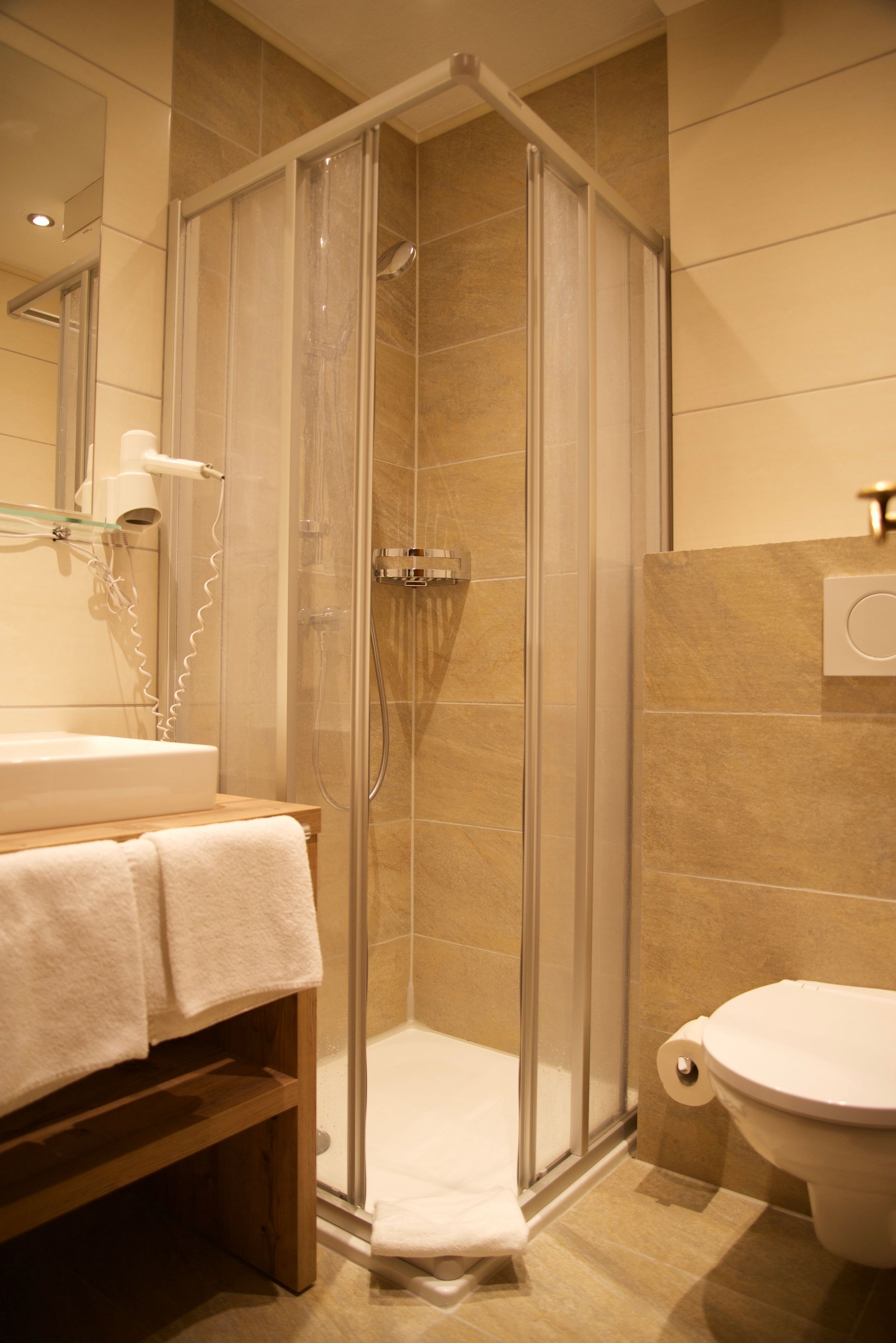 Kompaktes Badezimmer mit Eckdusche aus Glas, Waschbecken, Handtuchhalter und WC unter warmem Licht