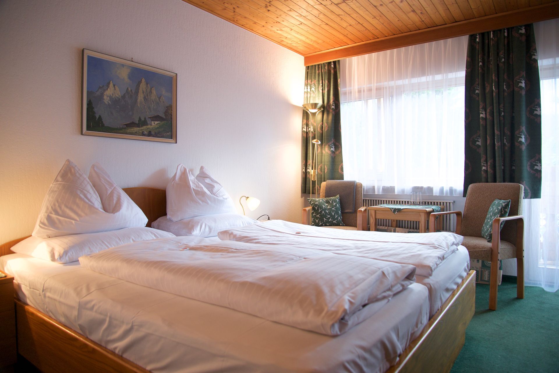 Gemütliches Hotelzimmer mit ungemachtem Bett, grünem Teppich, Fenster und kleiner Sitzecke