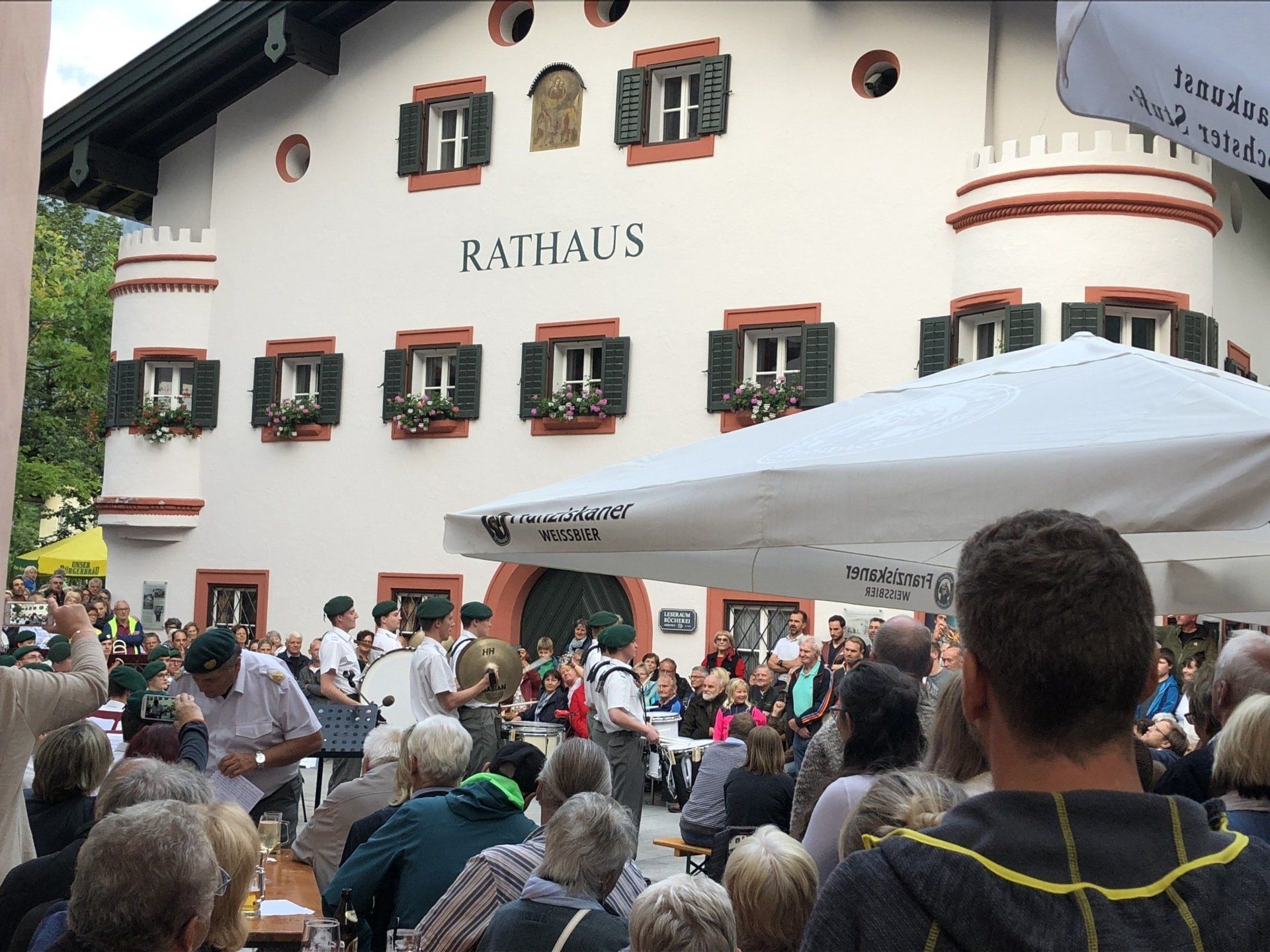 Während einer Freiluftveranstaltung versammelte sich eine Menschenmenge vor einem weißen Gebäude mit rot umrandeten Fenstern.