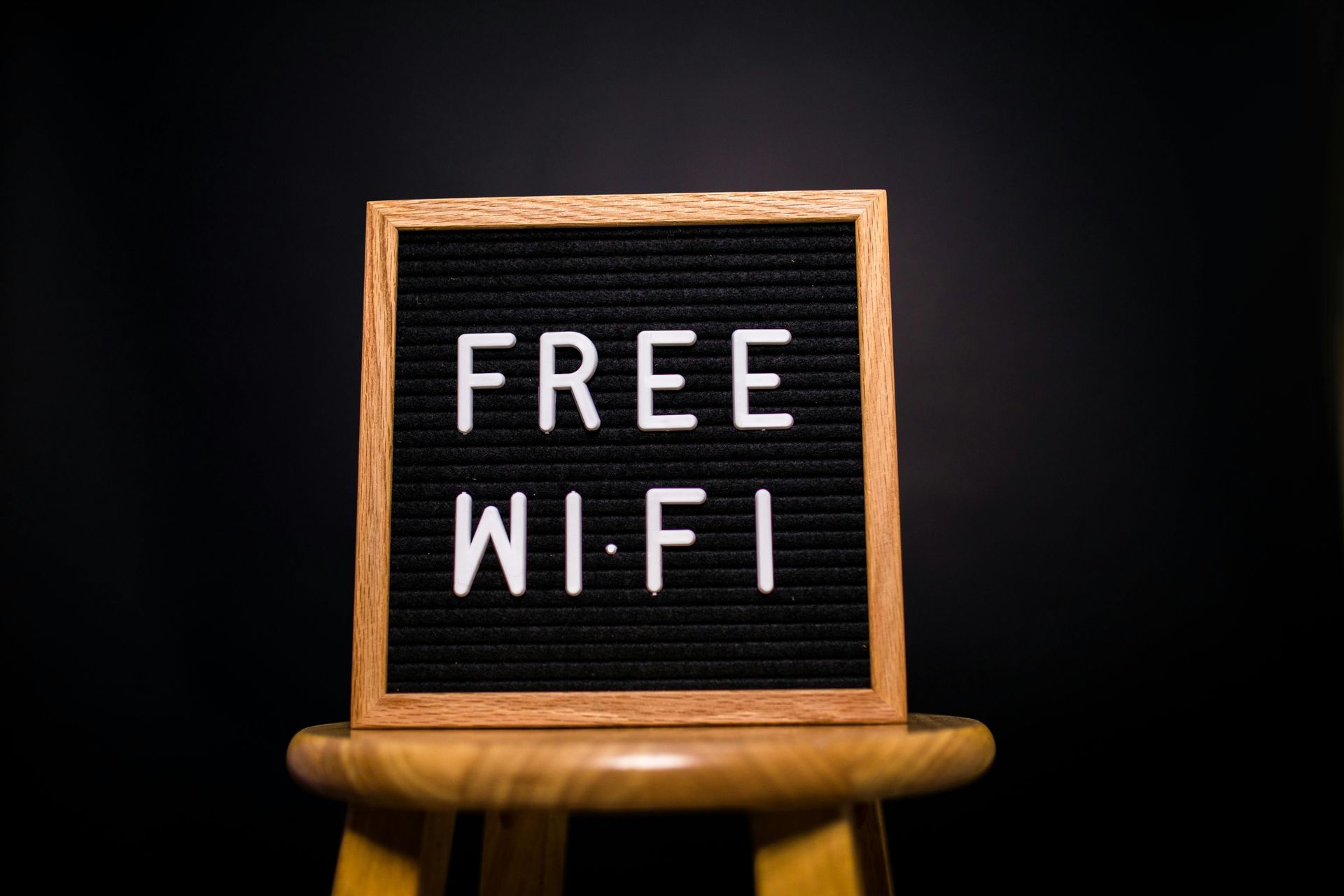 Kreidetafel auf einem Hocker mit der Aufschrift „KOSTENLOSES WLAN“ vor dunklem Hintergrund