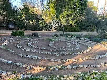 Tree Service El Monte Ca - A stone labyrinth in a sunlit garden, surrounded by lush greenery and trees. The scene is serene, with natural light casting soft shadows on the ground.