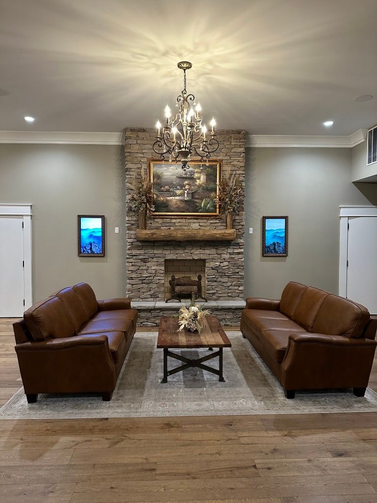 Elegant living room with two brown leather sofas facing a coffee table and stone fireplace under a chandelier