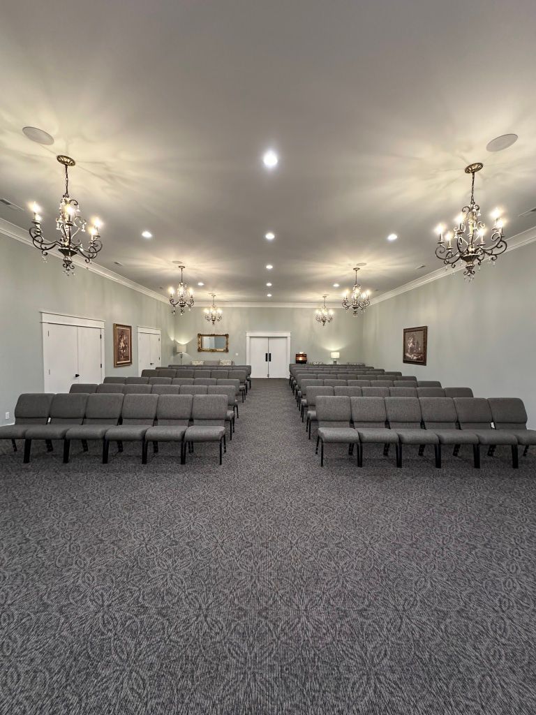 Empty event hall with gray chairs, chandeliers, and a central aisle under white walls and ceiling lights