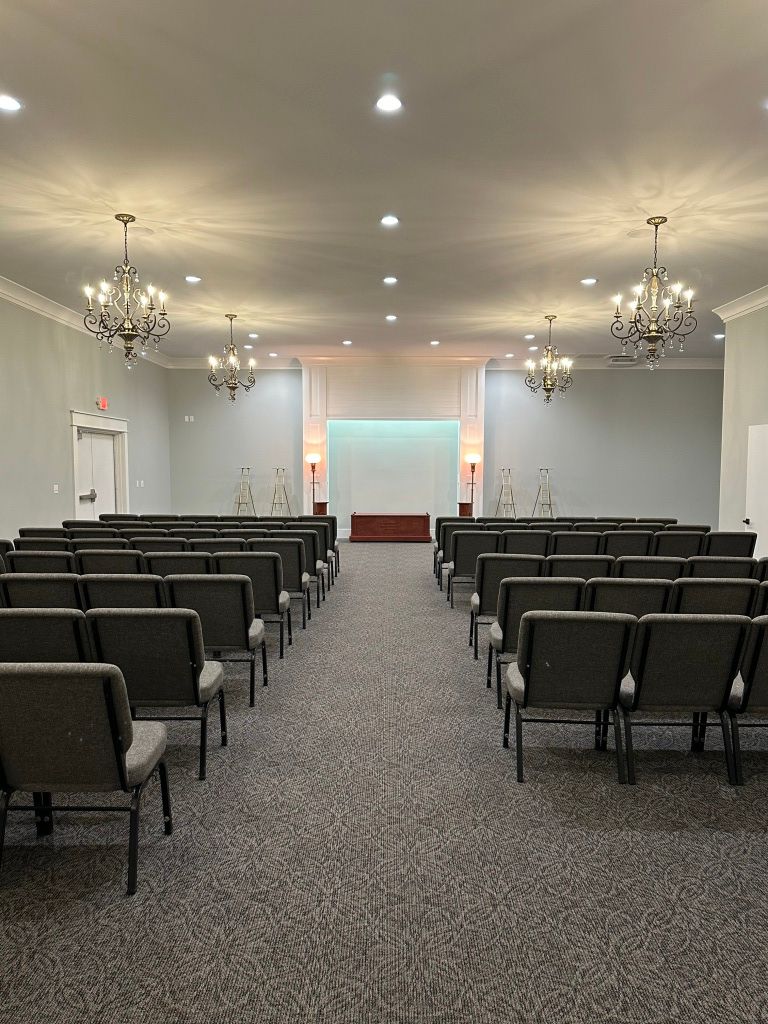Empty conference room with rows of black chairs, chandeliers, and a lit stage at the front