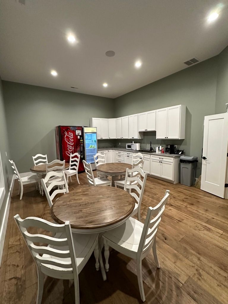 Spacious break room with round tables, white chairs, kitchen cabinets, and a red vending machine.