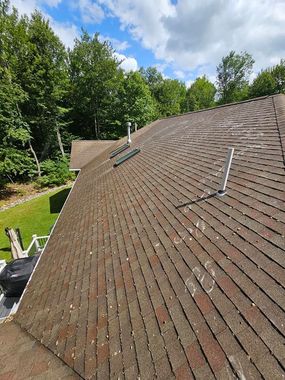 A person wearing safety gear pressure washes a tiled roof. A person wearing safety gear pressure washes a tiled roof.