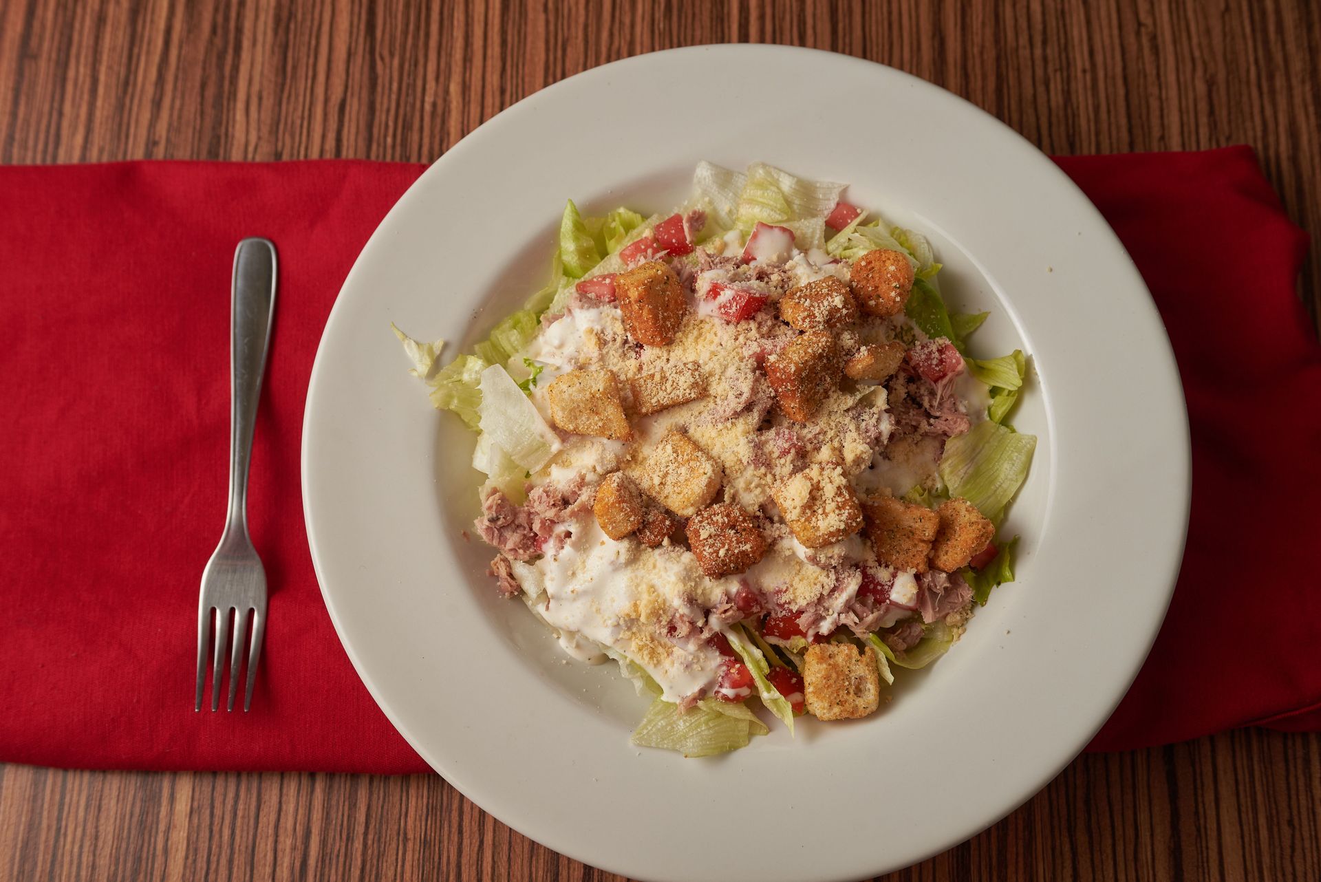 Caesar salad on a white plate with a fork, set on a red placemat on a wooden table