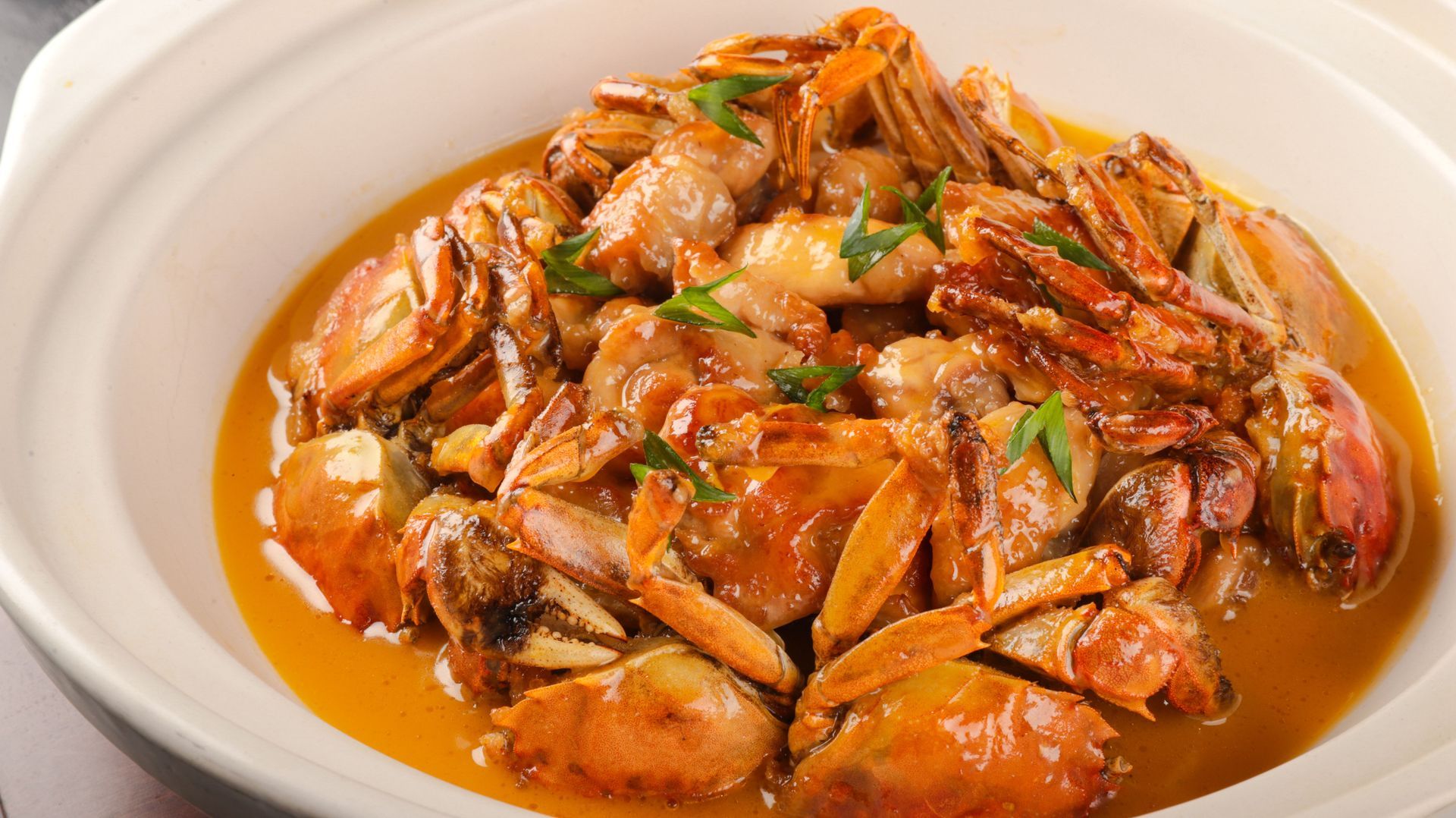 Crab pieces in spicy orange sauce, garnished with herbs, served on a white plate