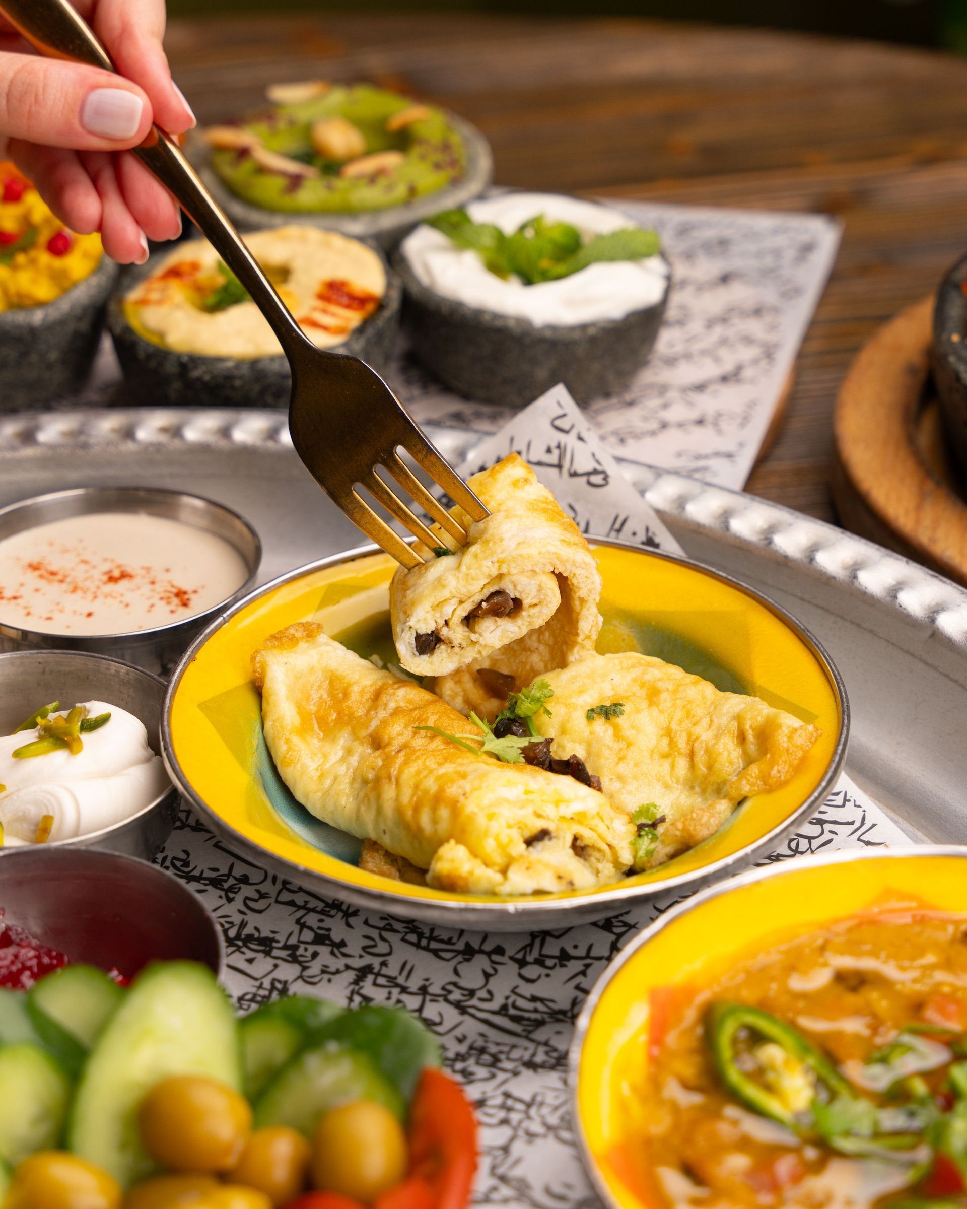Hand lifting a stuffed pastry from a yellow bowl, with assorted small dishes on a table