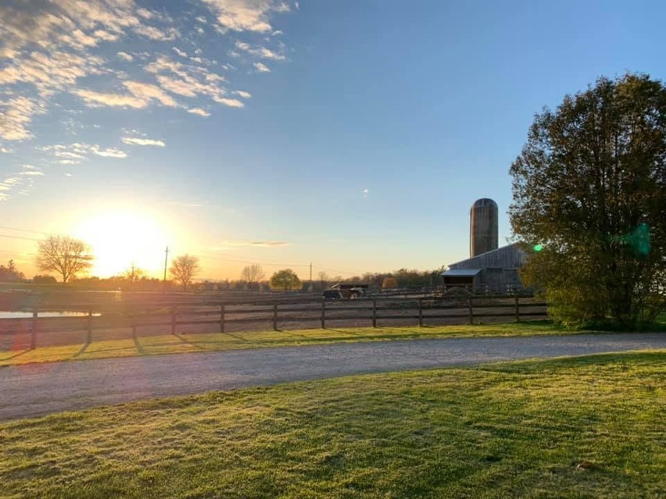 Sunset over a farm field with a barn, silo, fence, and grassy foreground