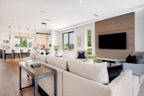 Bright open-plan living room with beige sectional, wall-mounted TV, and dining area in the background