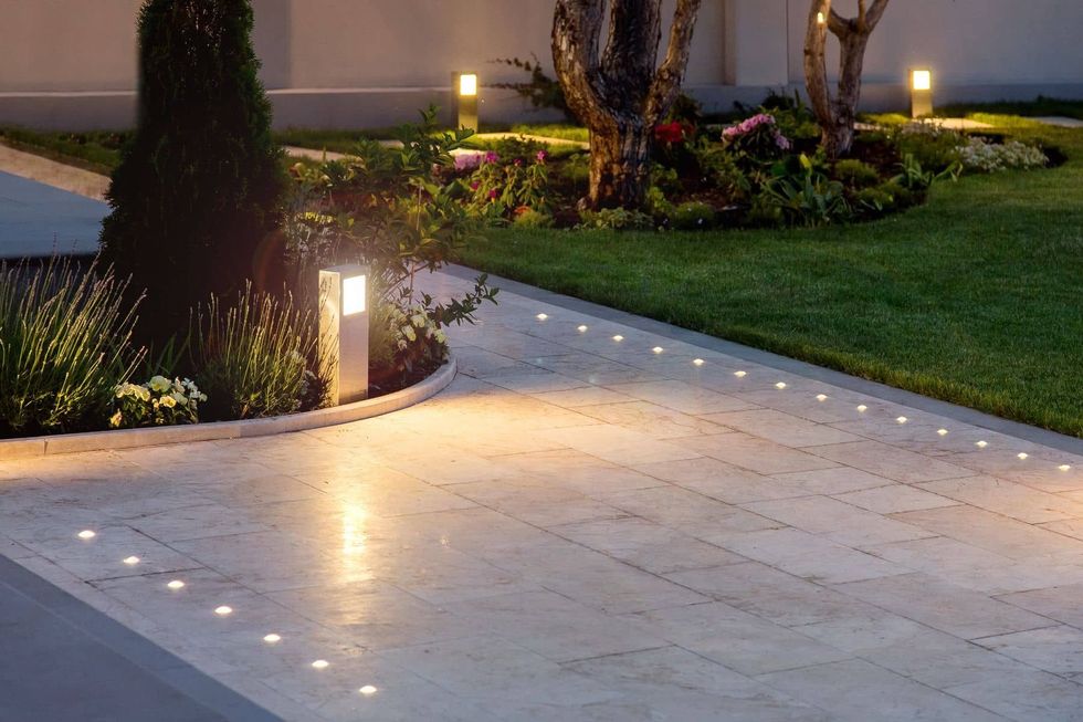 Illuminated garden walkway with in-ground lights, grass, and trees at dusk