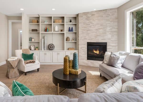 Modern living room with fireplace, built-in shelves, and beige seating around a round coffee table.