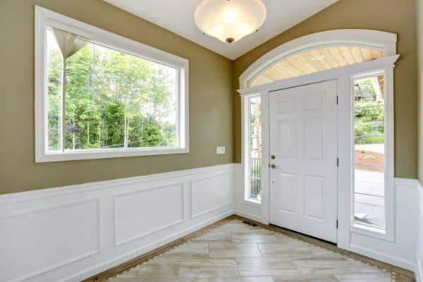 Bright foyer with white paneled walls, large window, front door, and tiled floor