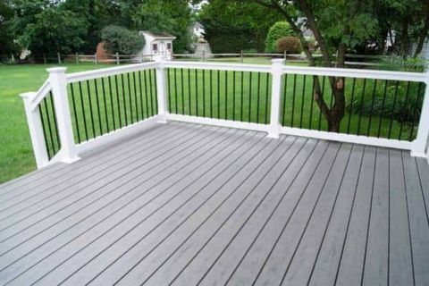 Gray wooden deck with white railing overlooking a green lawn and trees