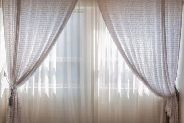 Sheer white curtains framing a bright window with pink drapes tied back on both sides