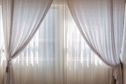 Sheer white curtains framing a bright window with pink drapes tied back on both sides