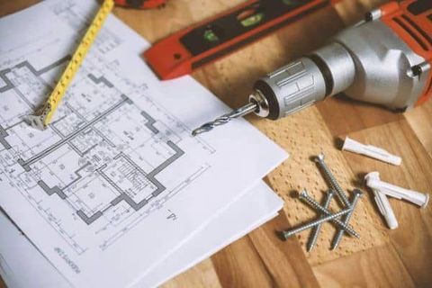 Drill, measuring tape, and blueprint on a wooden workbench for home renovation planning