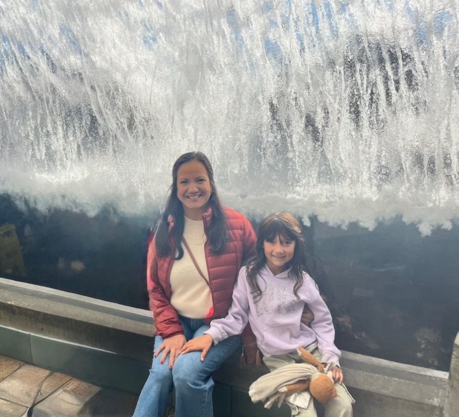 Two people sit on a bench in front of a large indoor waterfall, smiling at the camera.