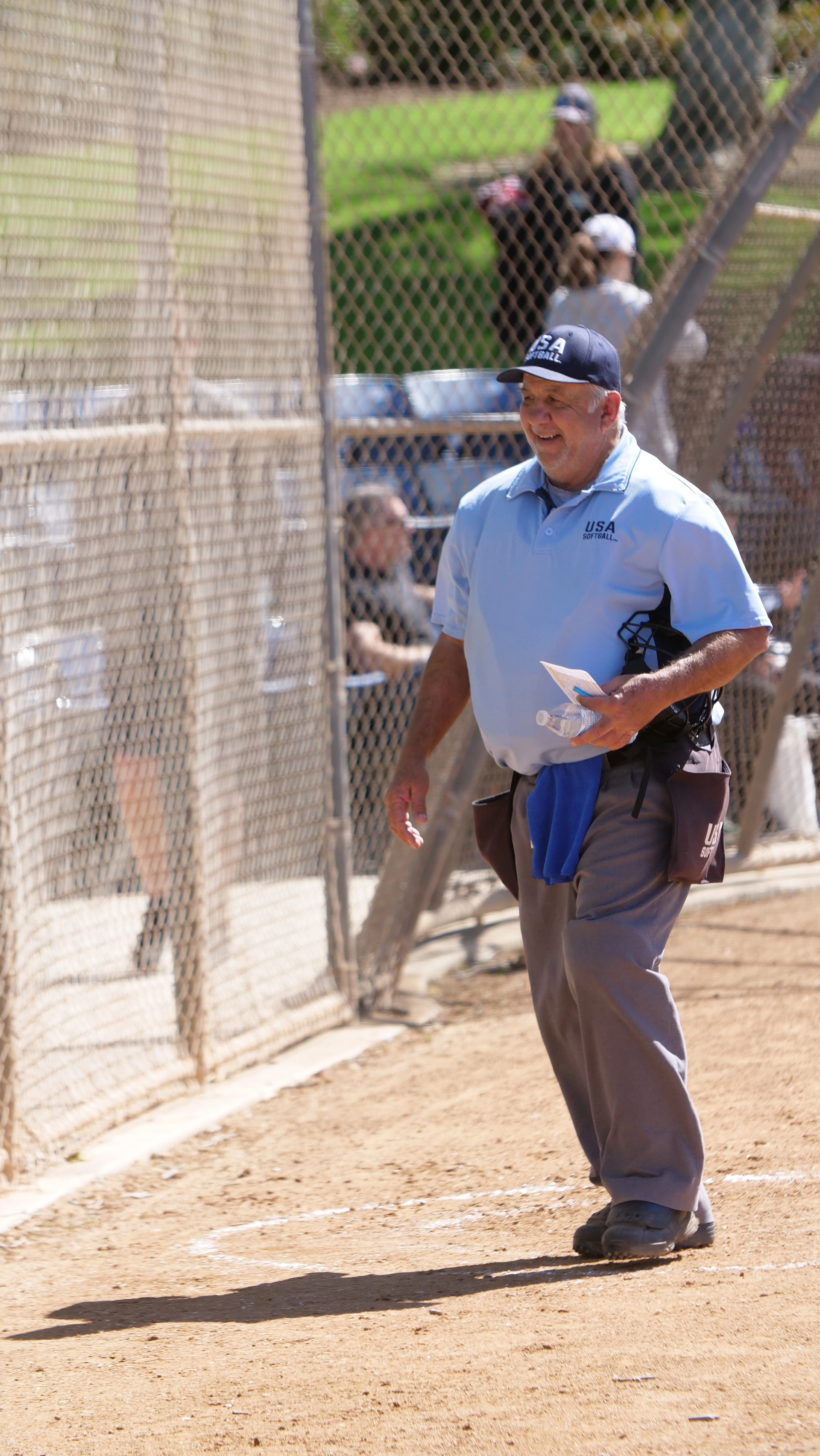 Baseball umpire in light blue shirt, gray pants, standing on a baseball field.