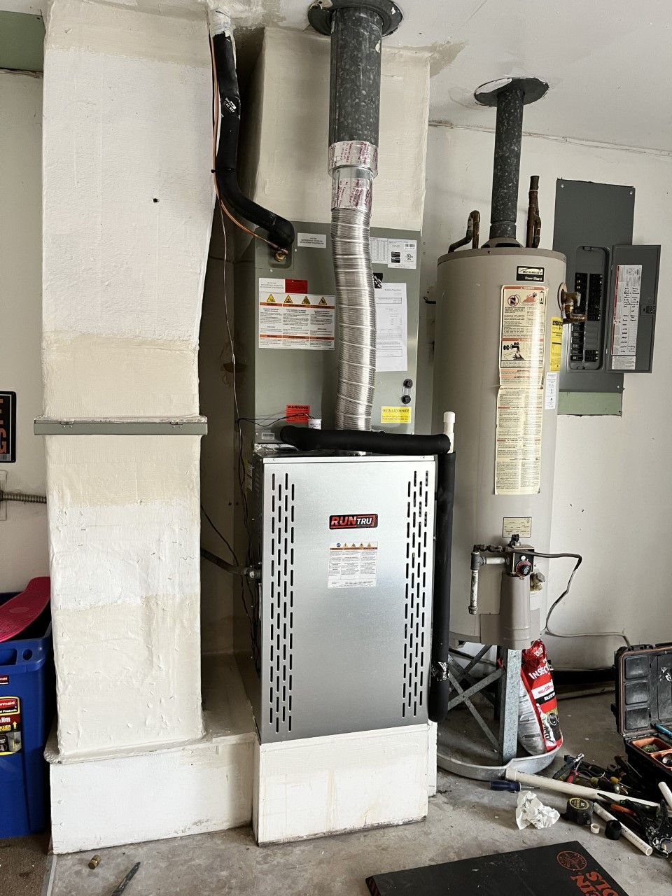 two water heaters are sitting next to each other in a garage by Astoria Heating & Cooling.