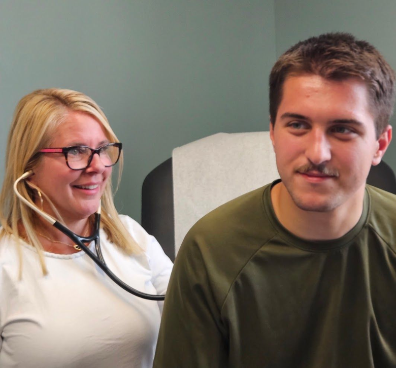 Doctor using a stethoscope to examine a seated patient in a clinic