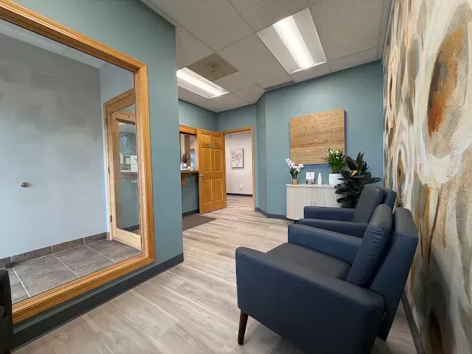 Modern office waiting area with blue chairs, light wood floors, a reception desk, and a large wall mirror