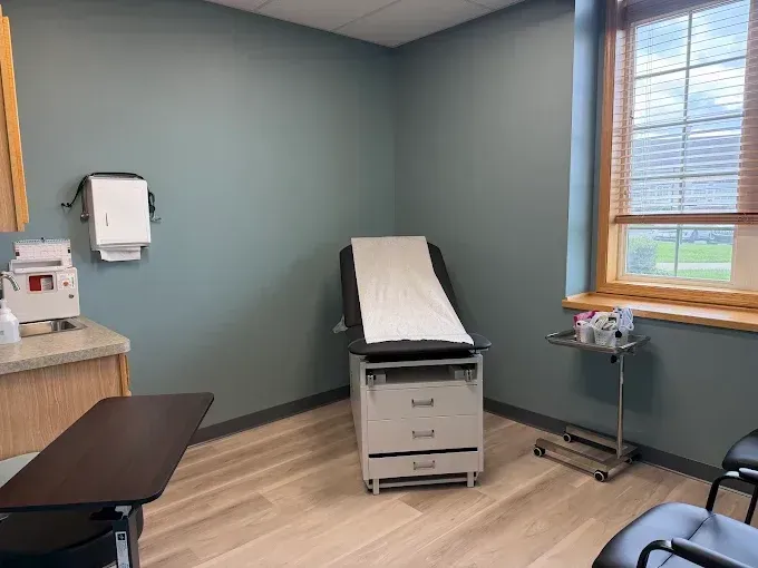 Medical exam room with exam table, sink, stool, and window with blinds